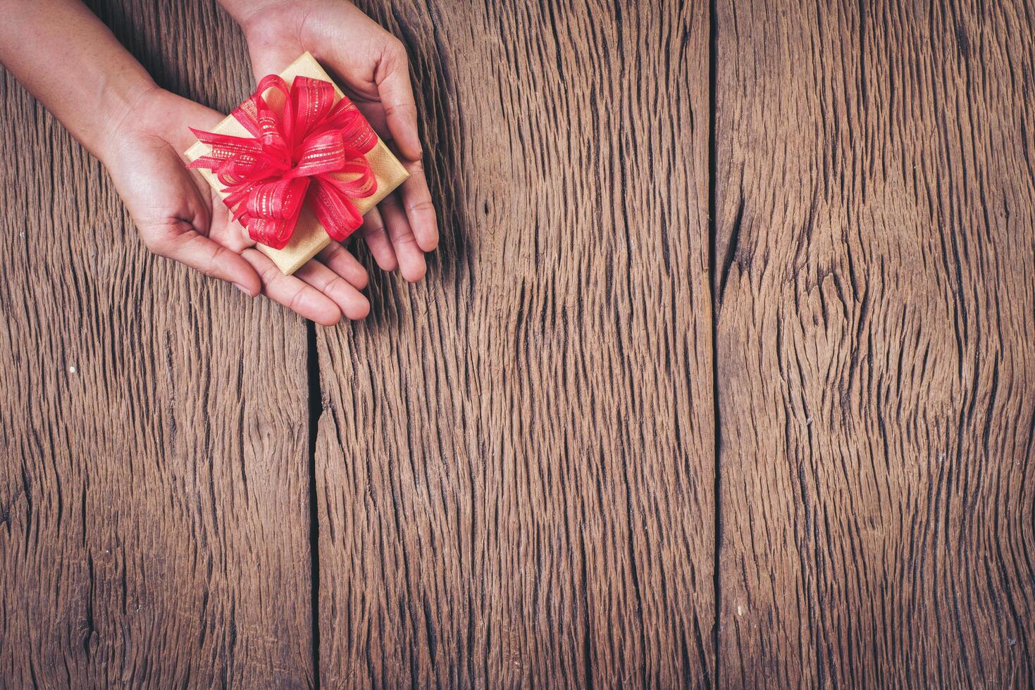 vista superior mano sujetando la caja de regalo sobre fondo de madera. foto