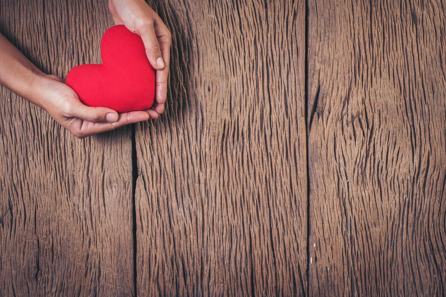 Hand holding red heart on wood background. photo