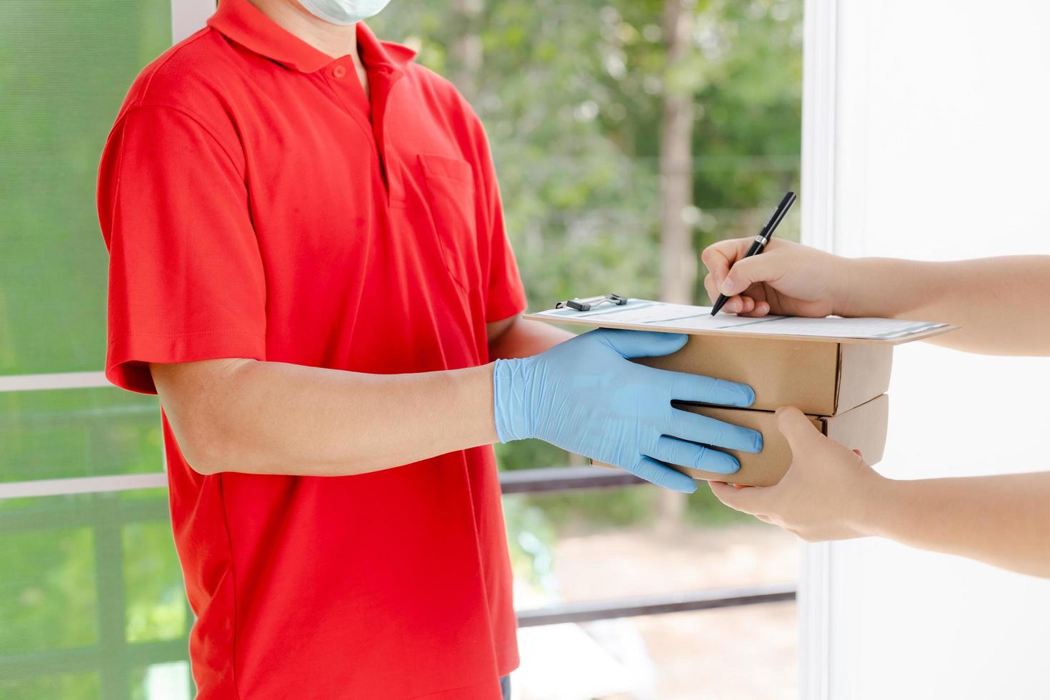 A delivery man wearing a red shirt and hat holds a parcel box photo