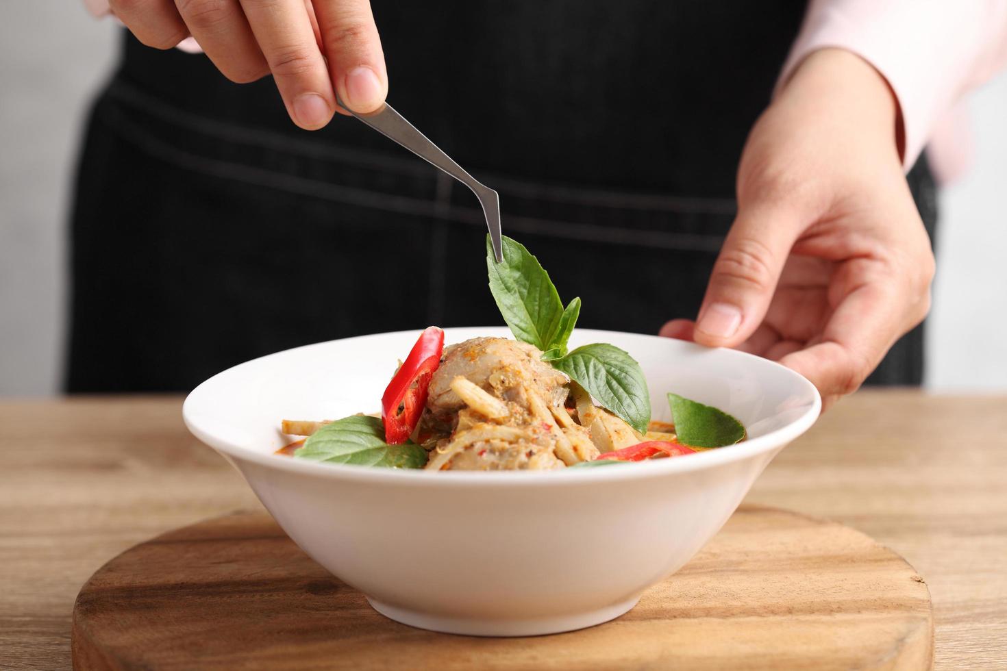 El estilista de alimentos usa pinzas para decorar la comida tailandesa en un plato blanco foto