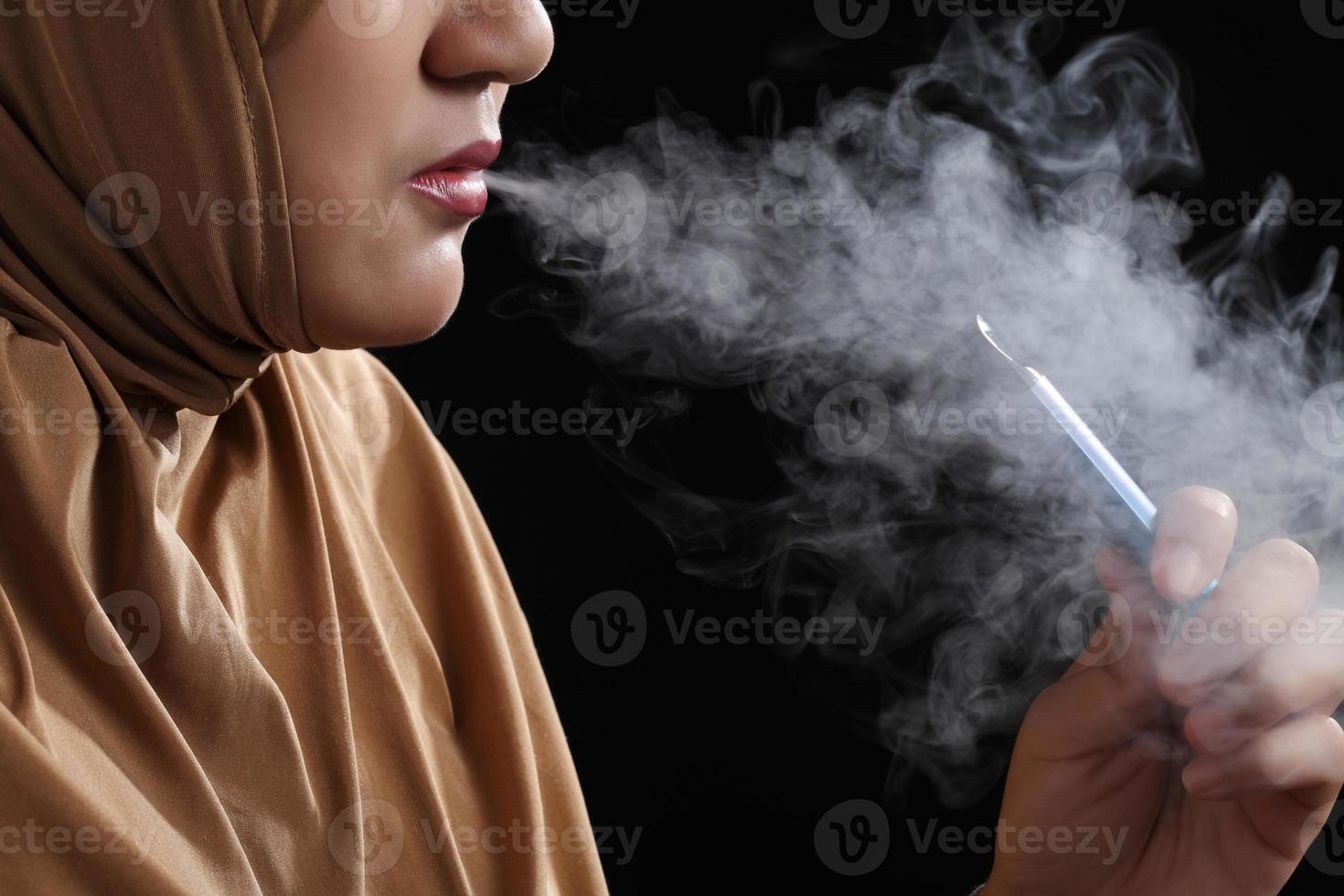 Cerrar joven mujer musulmana fumar cigarrillo electrónico sobre fondo negro foto