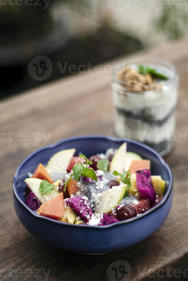 Ensalada de frutas exóticas asiáticas tropicales mixtas con semillas de albahaca y coco en un tazón al aire libre foto