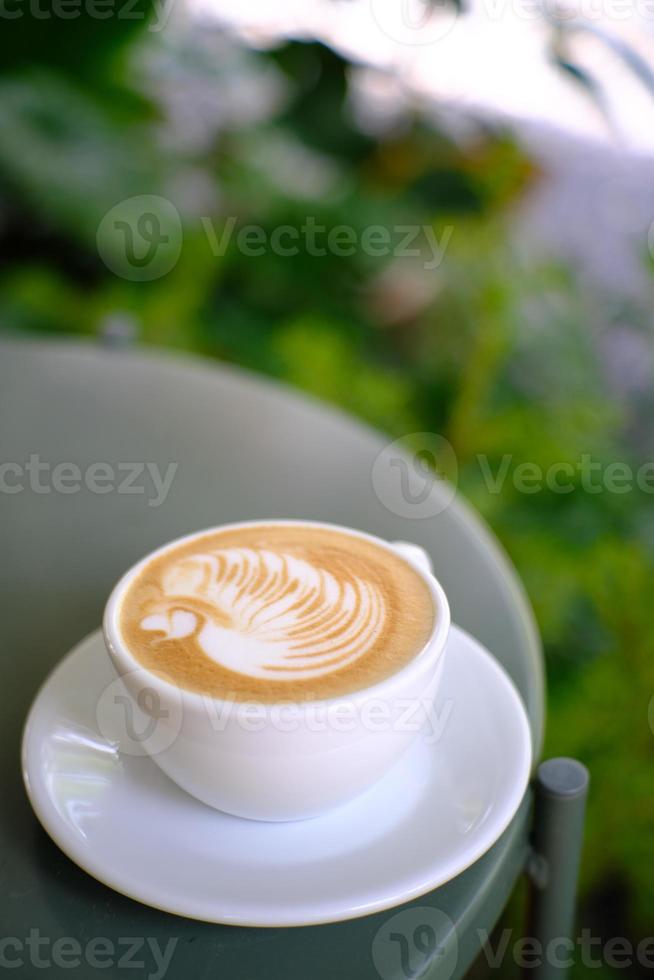 Coffee cup with latte art in a swan shape on the metal table photo
