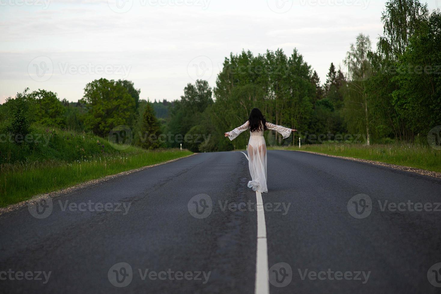 Rear view of a young woman standing on an empty asphalt country road photo