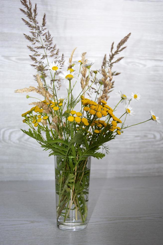 A bouquet of wildflowers in a glass vase on a wooden background photo