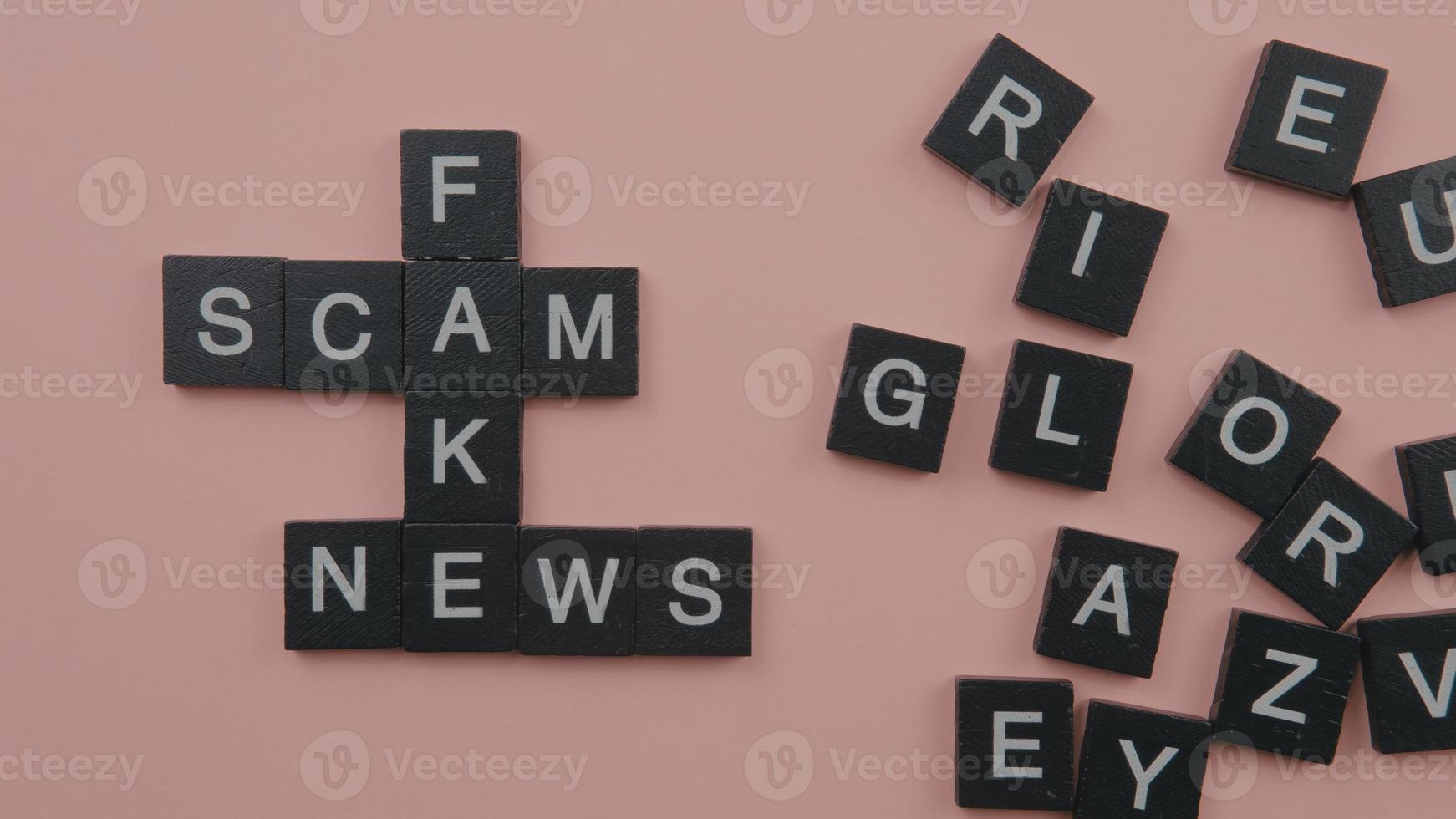 A group of scrabble tile forming word scam fake news. Selective focus on the tiles isolated on pink background photo