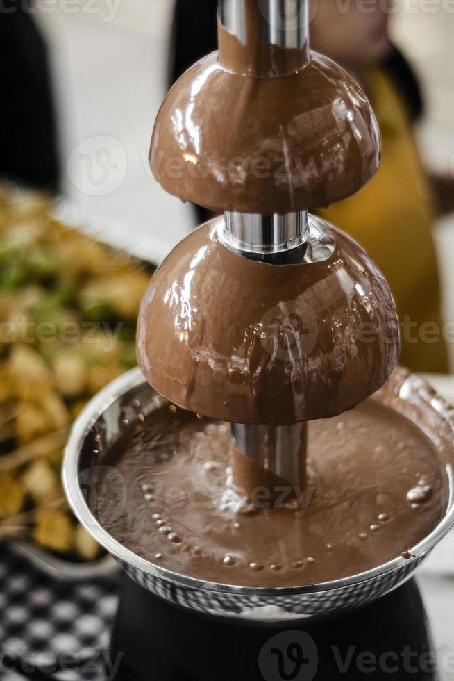 Fuente de chocolate, máquina de catering con brochetas de frutas en rústica mesa de buffet foto