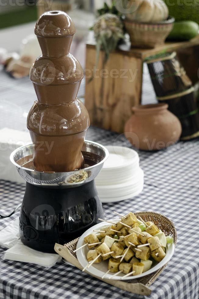 Chocolate fountain catering machine with fruit skewers on rustic buffet table photo