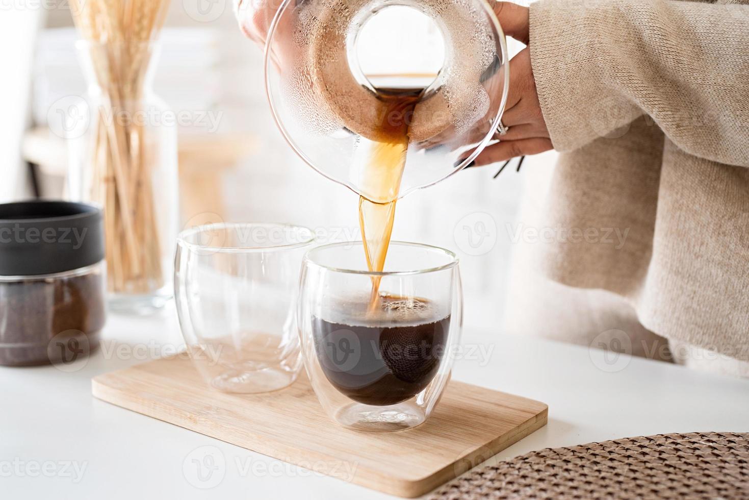 Mujer joven preparando café en una cafetera, vertiendo café en el vaso foto