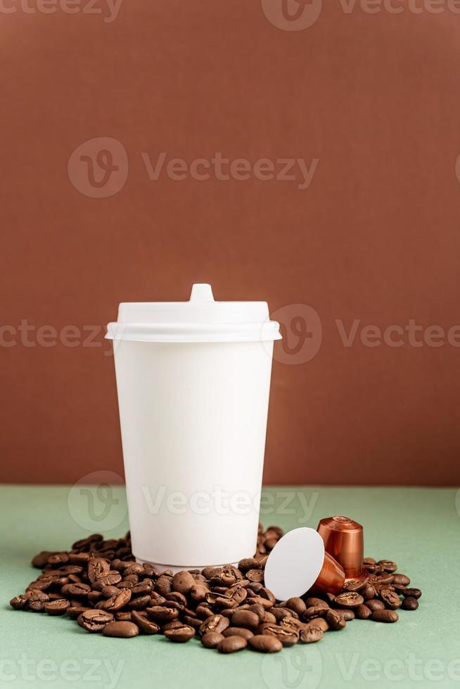 Vaso de papel blanco desechable ecológico con granos de café y cápsulas foto
