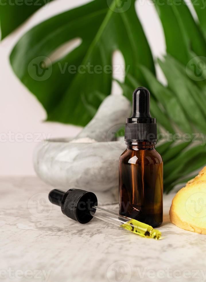 tubo con aceite esencial rodeado de jengibre, sal, hojas tropicales foto