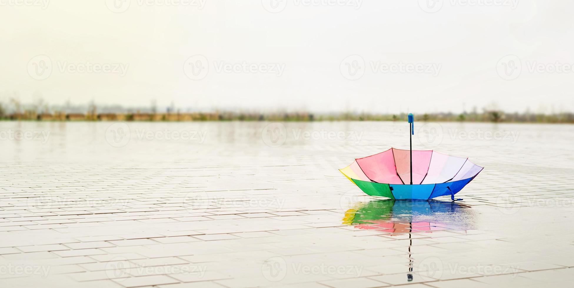 Rainbow colored umbrella lying in puddles on the wet street ground photo