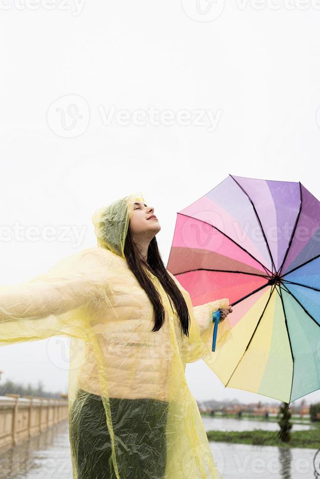 Beautiful brunette woman holding colorful umbrella dancing in the rain photo