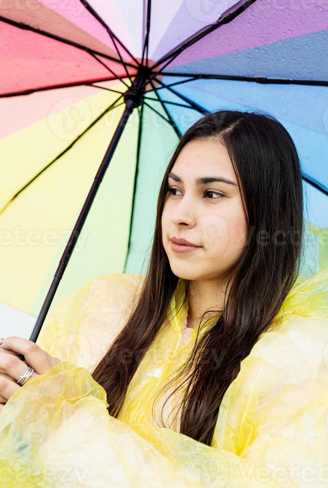 Beautiful brunette woman holding colorful umbrella out in the rain photo