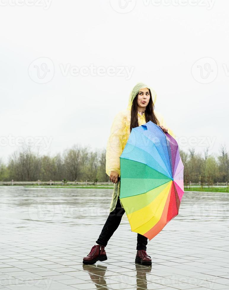 Beautiful brunette woman holding colorful umbrella out in the rain photo