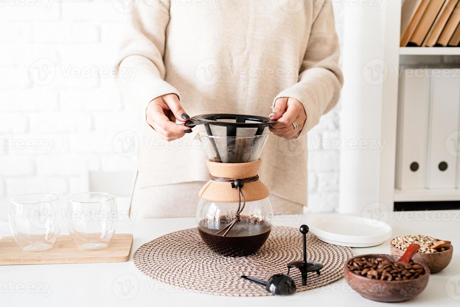 Mujer joven preparando café en una cafetera, vertiendo café en el vaso foto