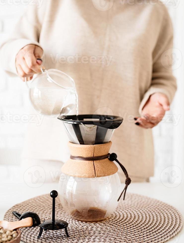 Mujer preparando café en una cafetera, vertiendo agua caliente en el filtro foto