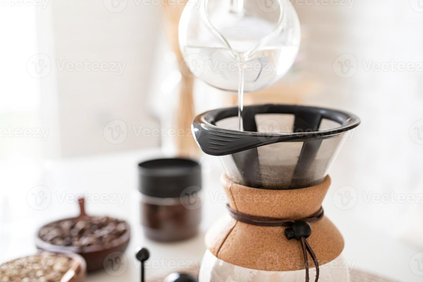Mujer preparando café en una cafetera, vertiendo agua caliente en el filtro foto