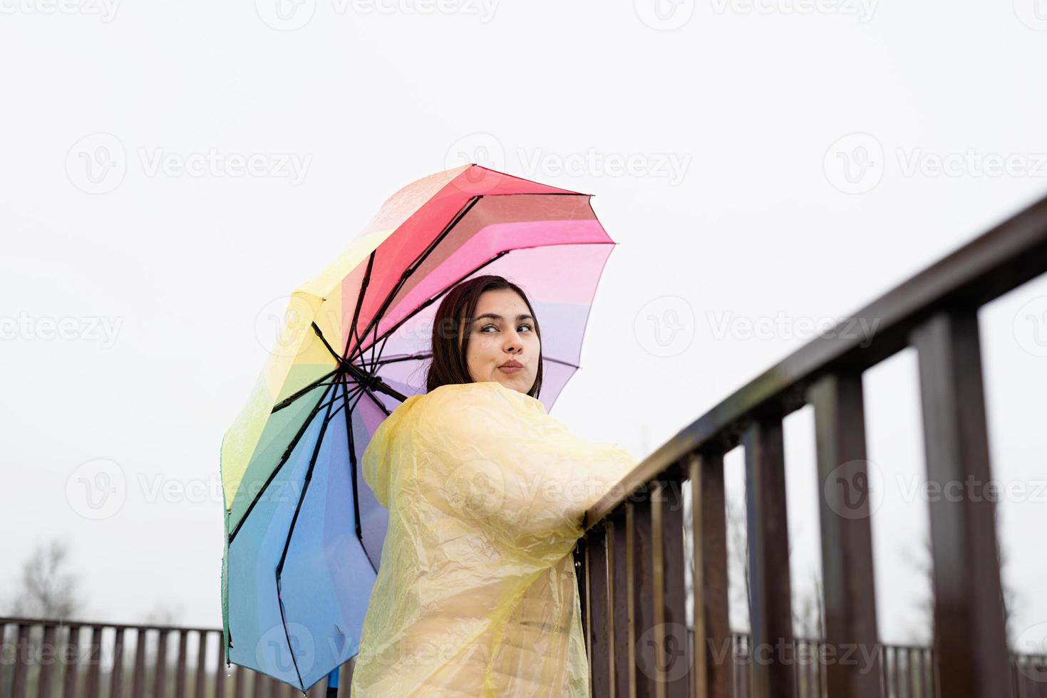 Mujer de pie afuera sosteniendo un paraguas de colores, mirando a otro lado foto