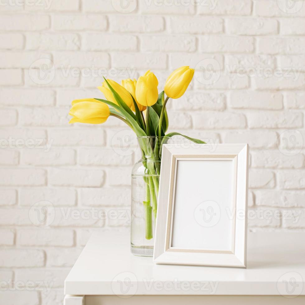 Yellow tulips in a glass vase and blank photo frame