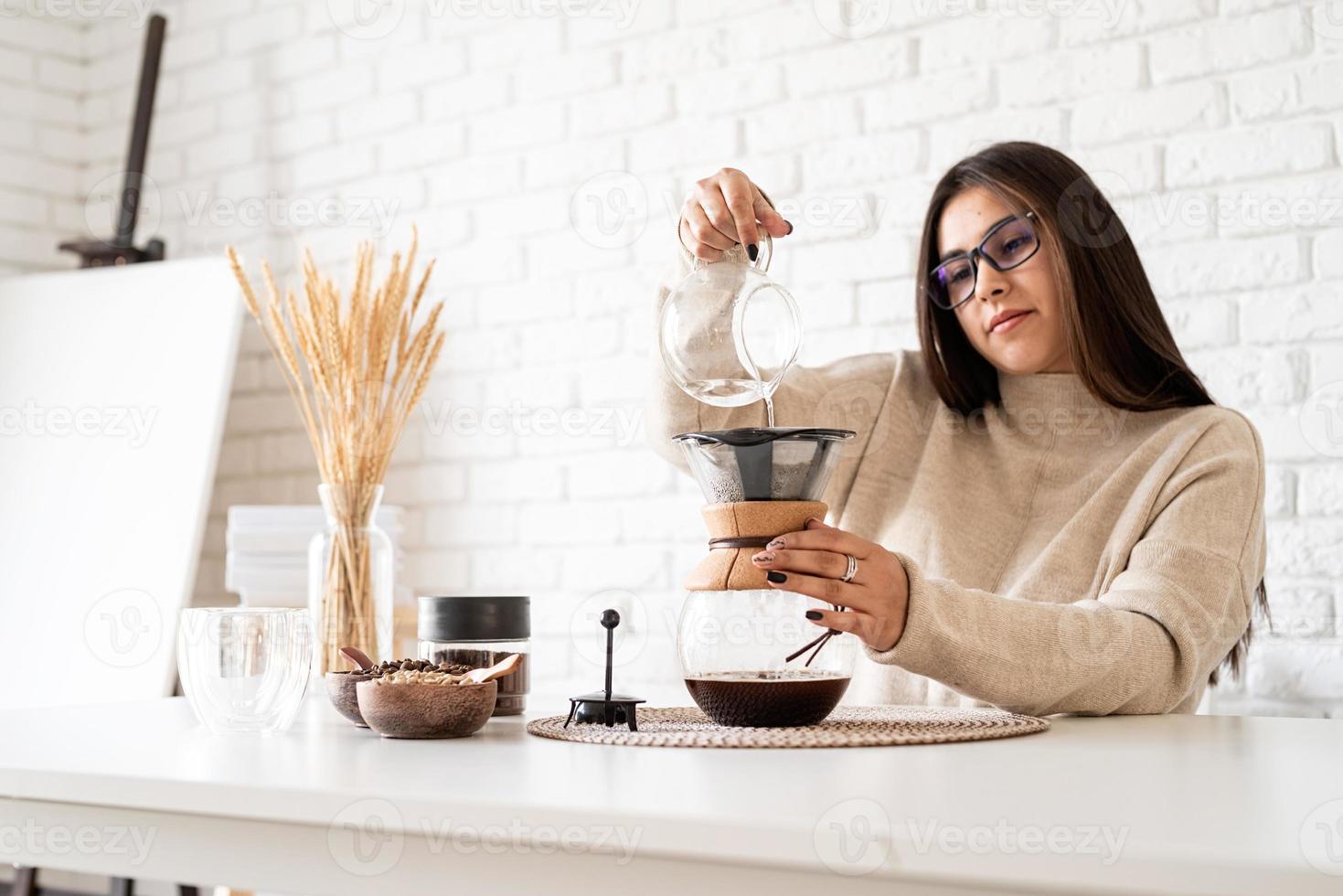 Mujer preparando café en una cafetera, vertiendo agua caliente en el filtro foto