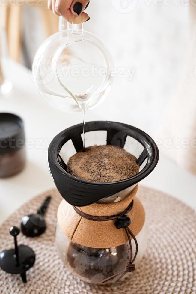 Mujer preparando café en una cafetera, vertiendo agua caliente en el filtro foto