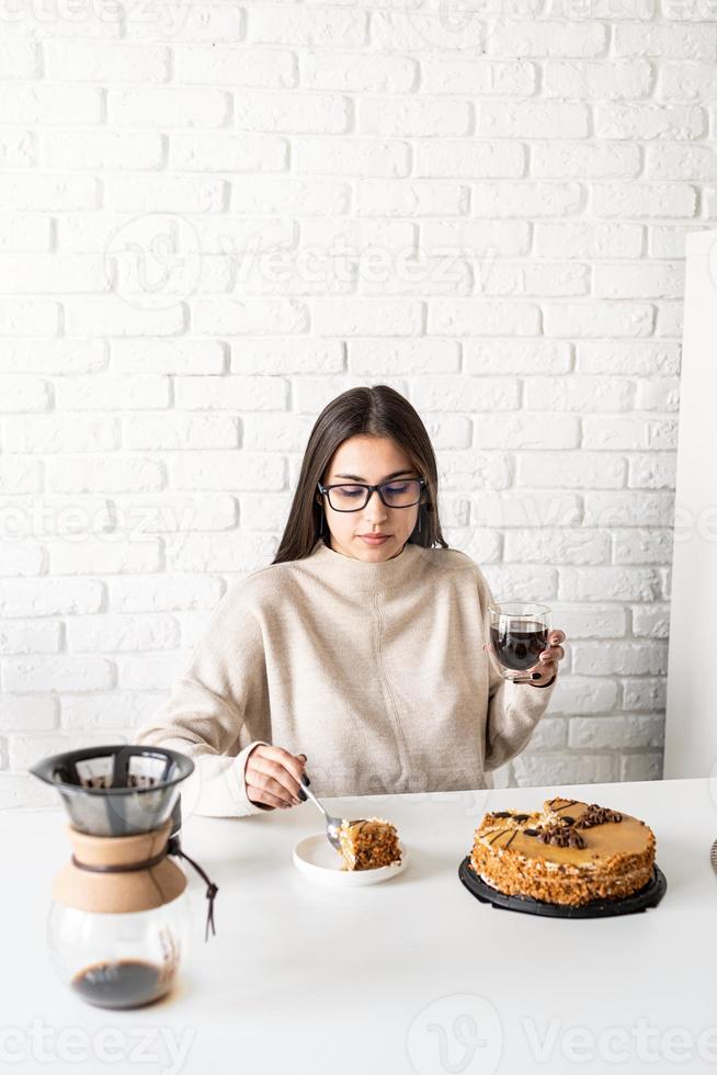 mujer sentada en la mesa blanca, comiendo pastel y tomando café foto