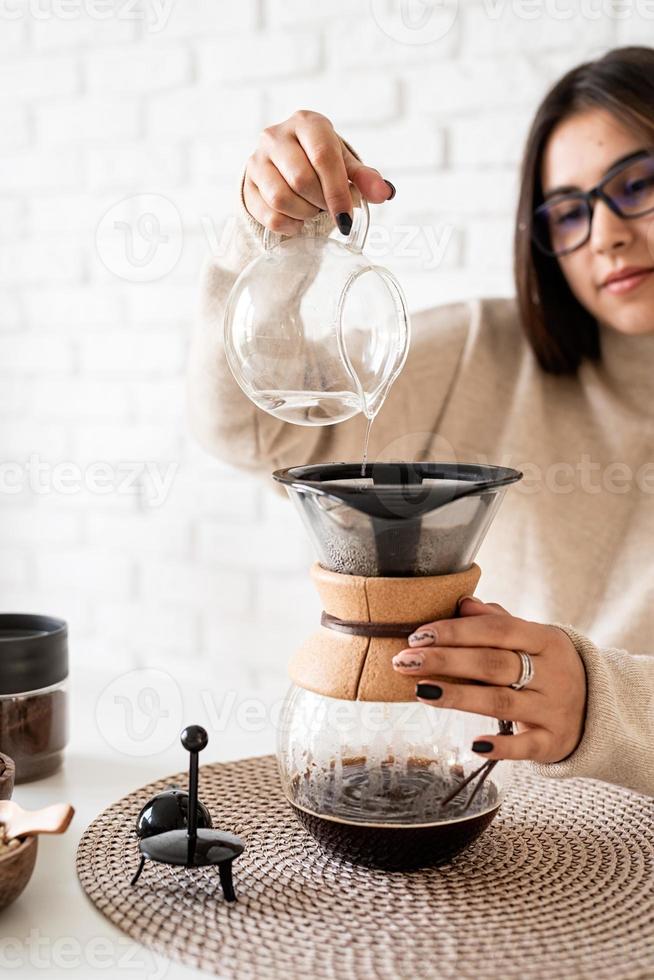 Mujer preparando café en una cafetera, vertiendo agua caliente en el filtro foto