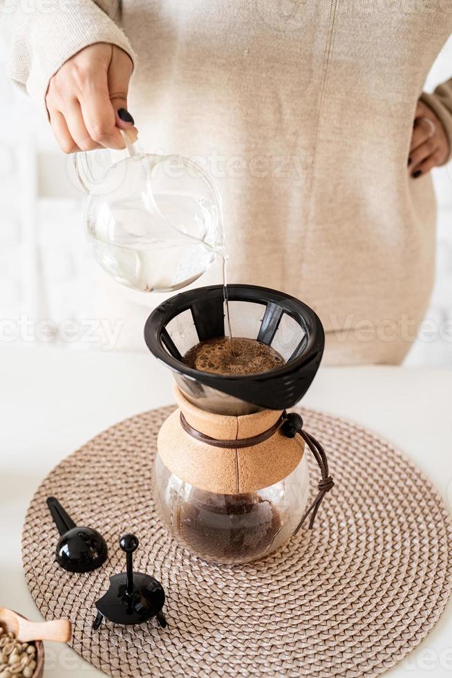 Mujer preparando café en una cafetera, vertiendo agua caliente en el filtro foto