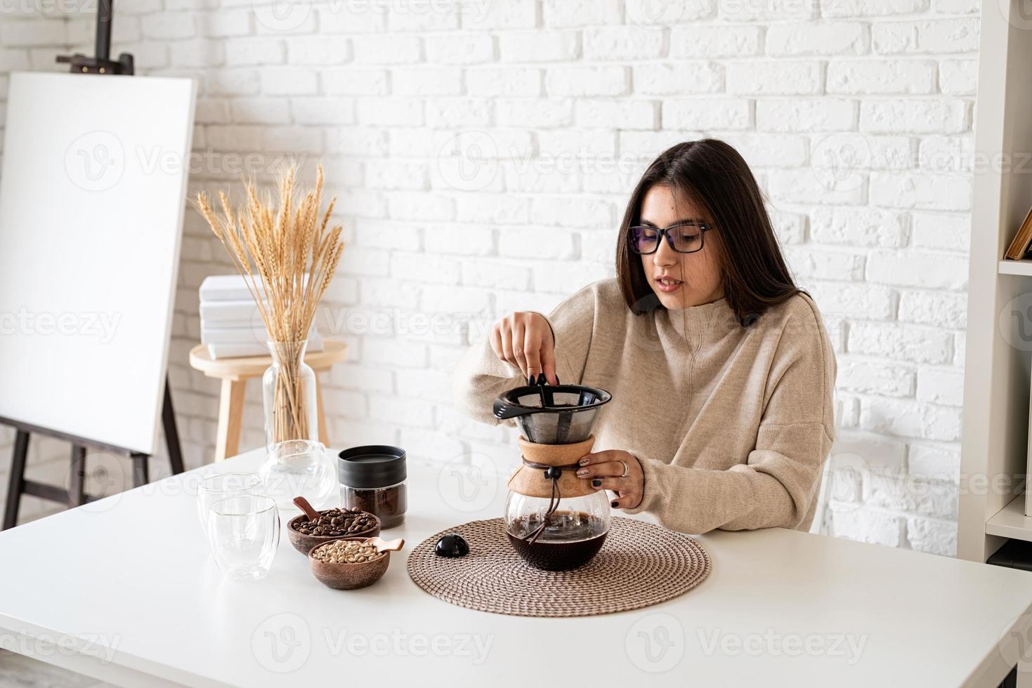 Mujer preparando café en una cafetera, vertiendo agua caliente en el filtro foto