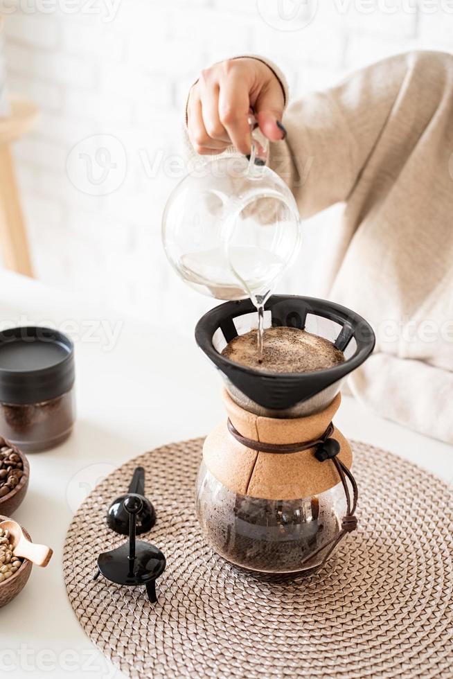 Mujer preparando café en una cafetera, vertiendo agua caliente en el filtro foto