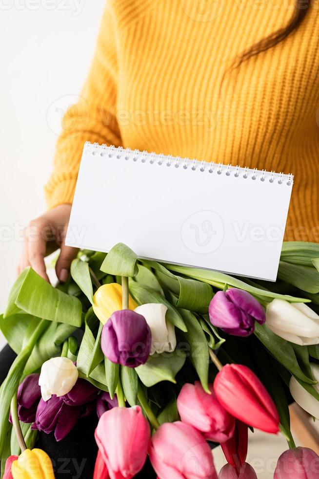 Mujer con ramo de tulipanes rosas frescos y calendario en blanco para maqueta foto