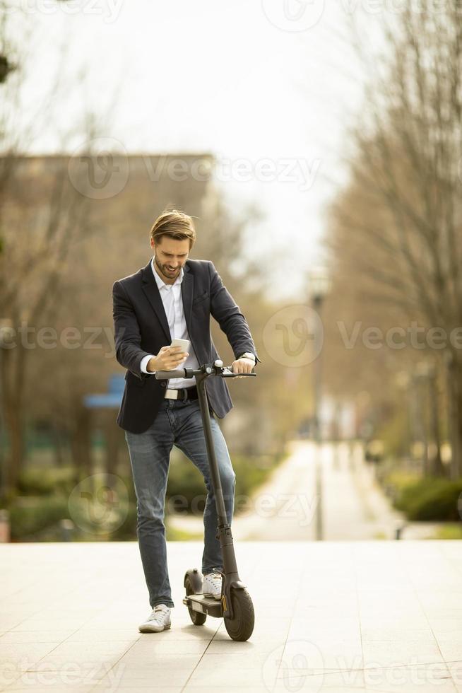 Young businessman using mobile phone  on electric scooter photo
