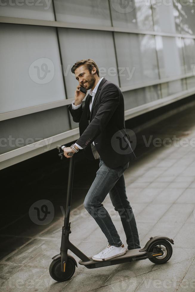 Joven empresario mediante teléfono móvil en scooter eléctrico foto