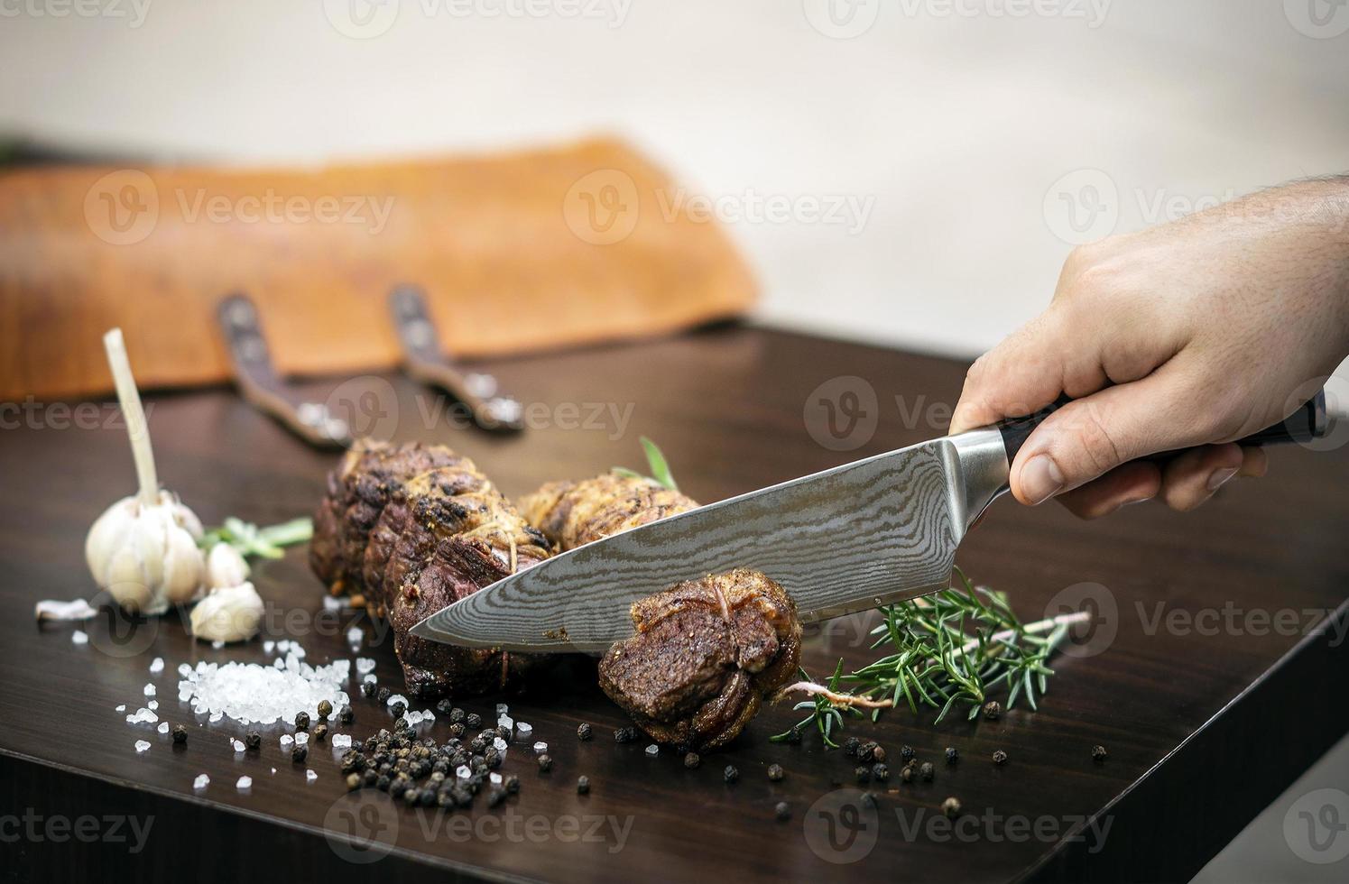 Slicing a serving of organic roast beef roll with knife on wood table with garlic pepper and salt in Melbourne Australia photo