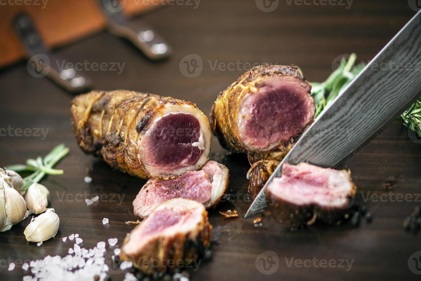Slicing a serving of organic roast beef roll with knife on wood table with garlic pepper and salt in Melbourne Australia photo