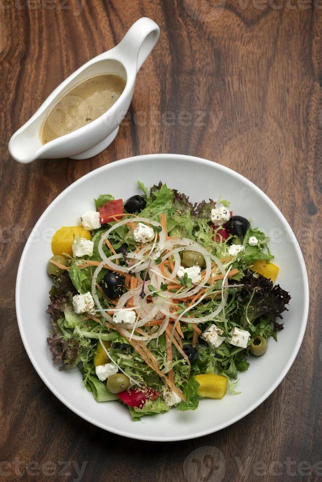 Greek salad with feta cheese and olives with citrus vinaigrette on wooden table photo