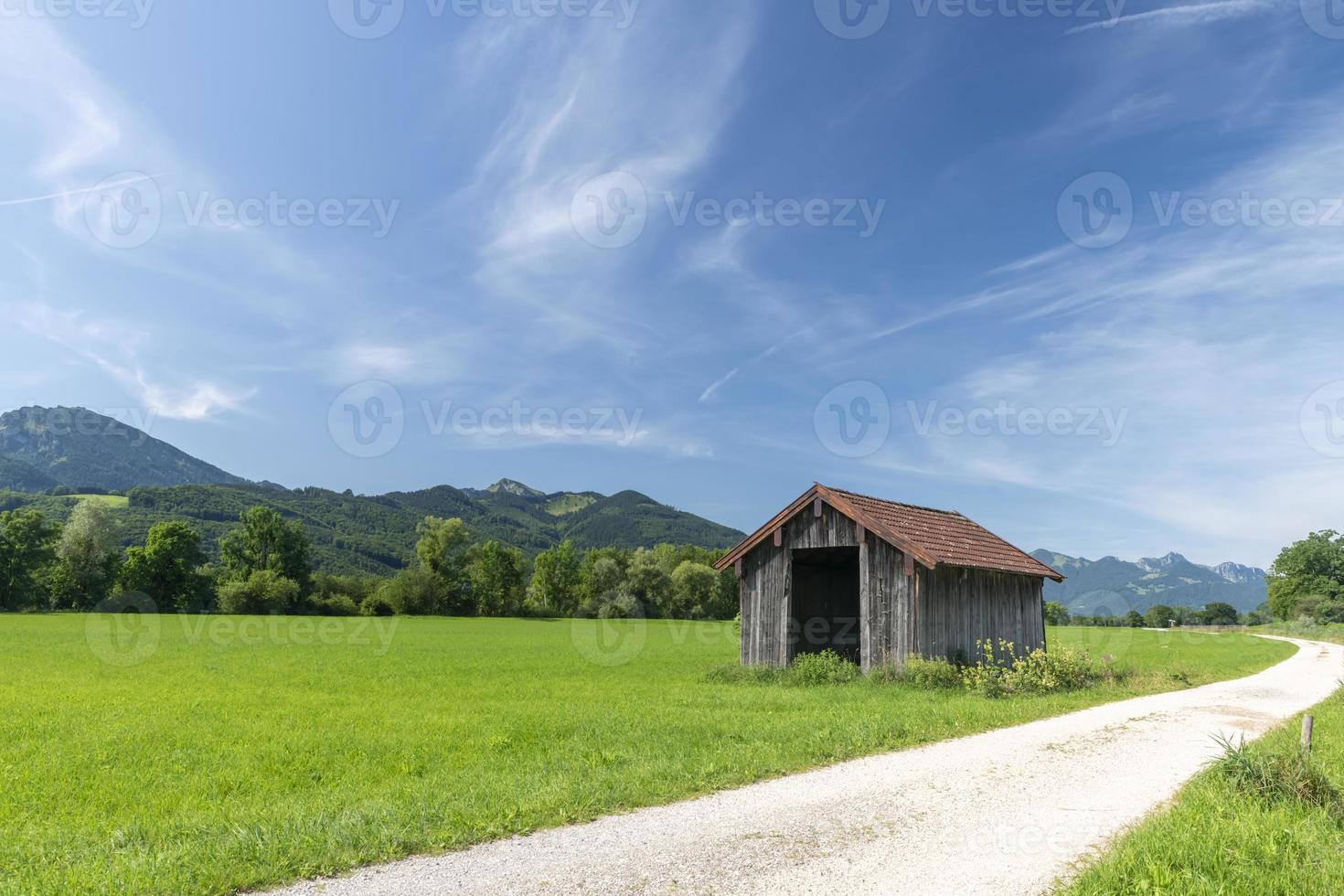 Paisaje de pradera bávara con cabaña de madera, camino de luz y cielo azul foto