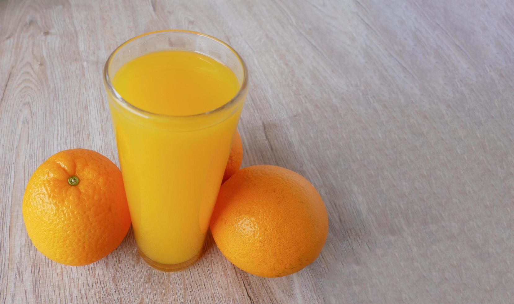 Glass of orange juice and oranges on wooden floor photo