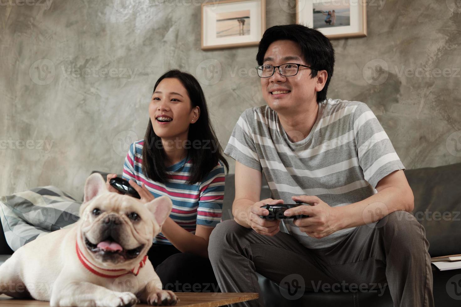 pareja asiática está jugando videojuegos y un perro mascota cerca. foto