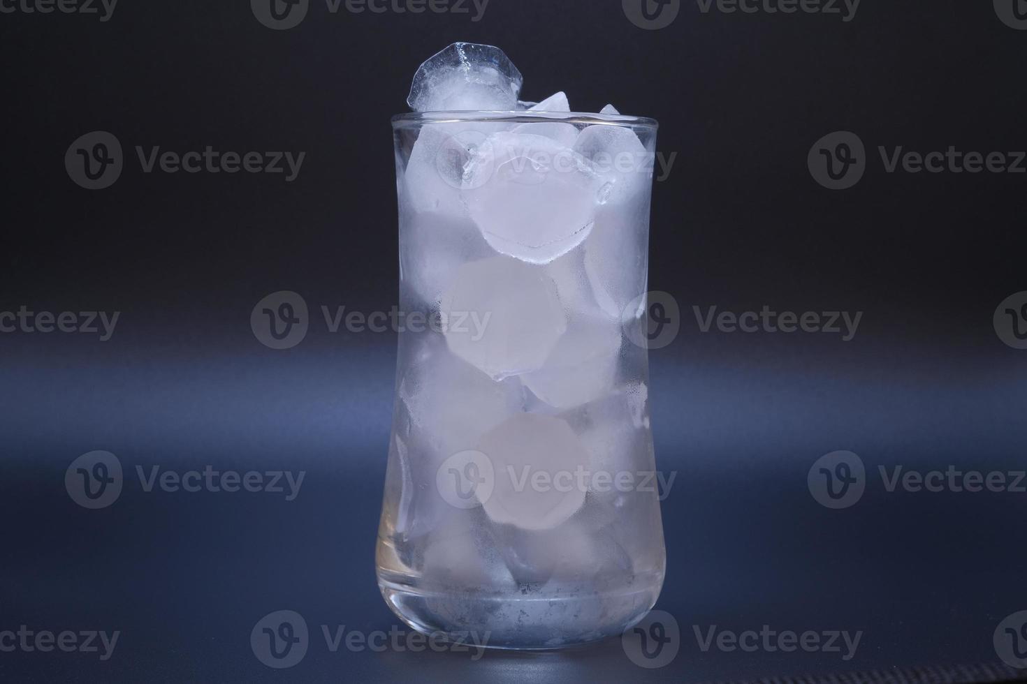 El hielo en un vaso de agua transparente se derrite sobre fondo negro. foto