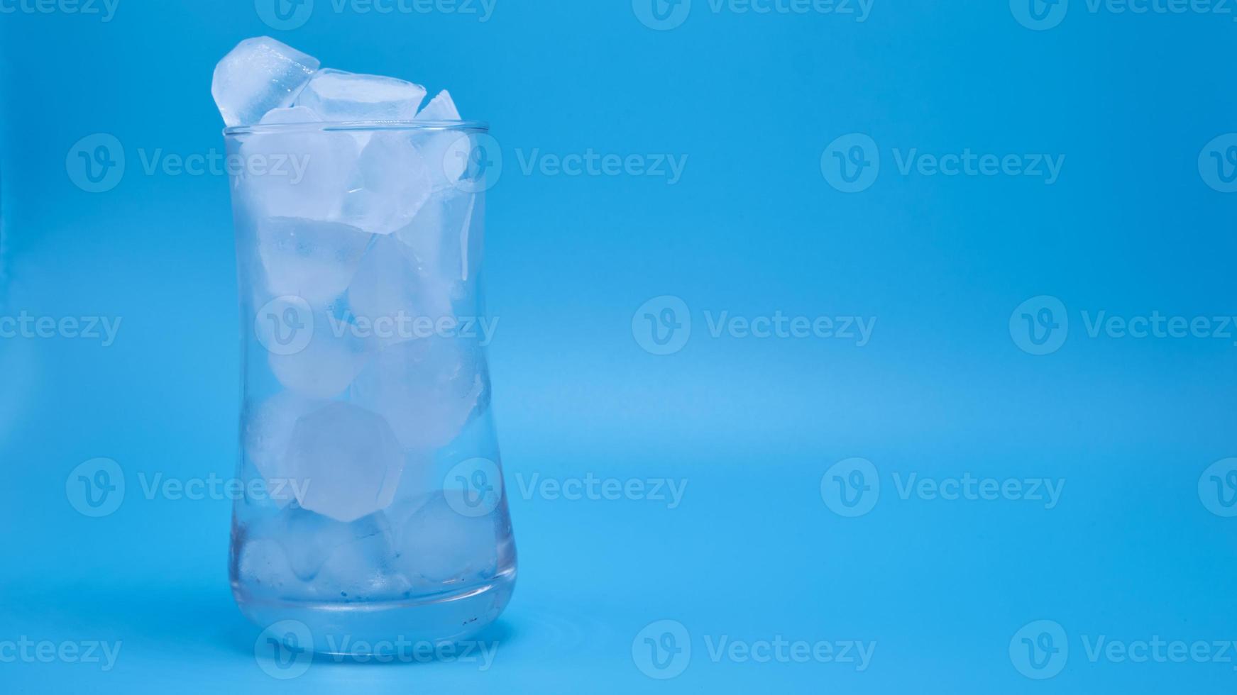 el hielo en un vaso de agua transparente derritiéndose sobre fondo azul. foto