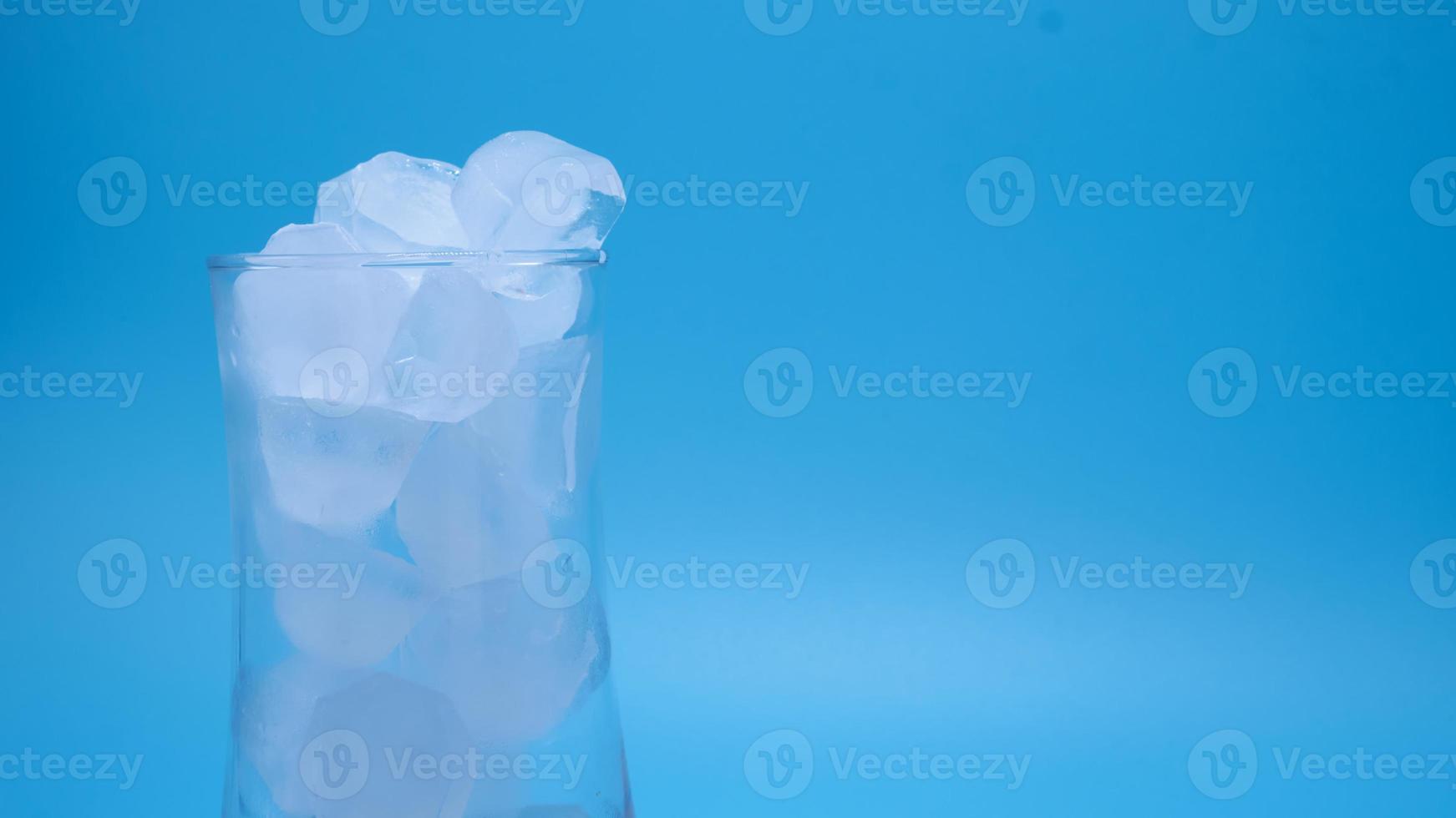 The ice in clear glass of water melting on blue background. photo