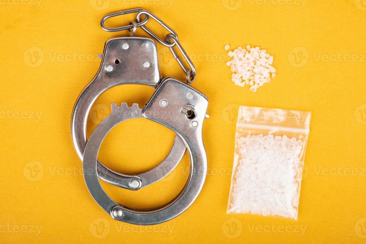 Crystal drugs and handcuffs on yellow background, white powder drug trafficking. photo