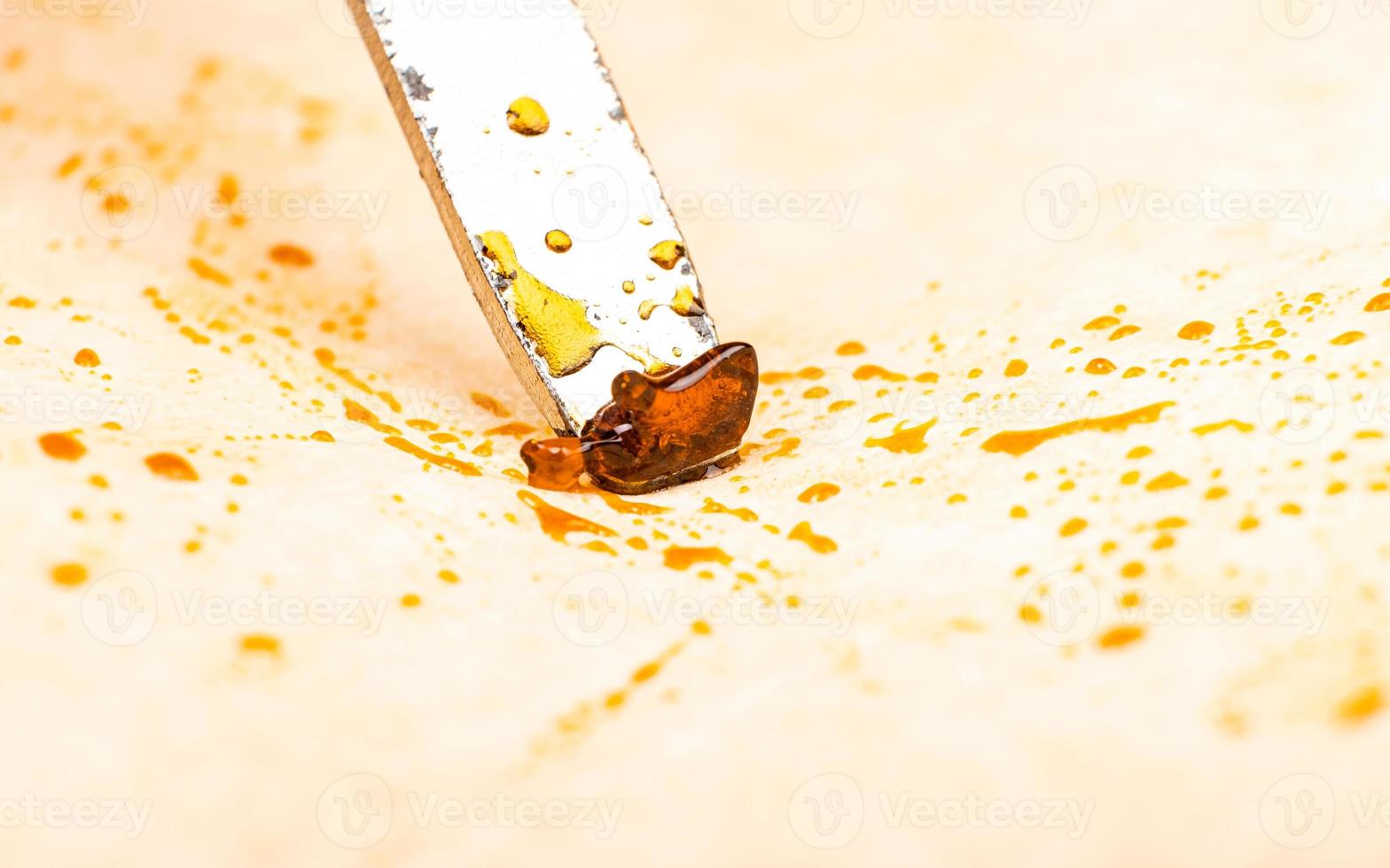 Scrape the golden cannabis wax off the parchment paper with dab tool. photo