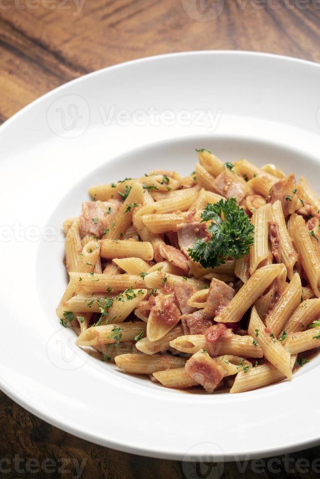 Penne amatriciana pasta con salsa de tomate y jamón sobre fondo de tabla de madera foto