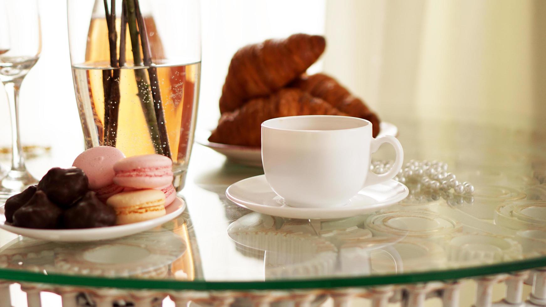 Glass table with a cup of coffee, sweet croissants photo