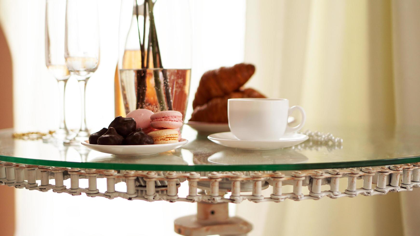 mesa de cristal con una taza de café, croissants dulces foto