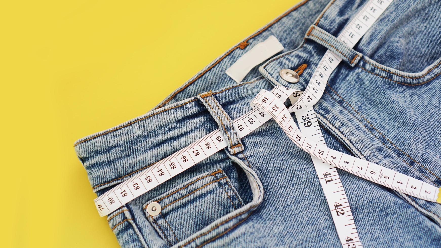 Measuring tape and jeans on a bright yellow background photo