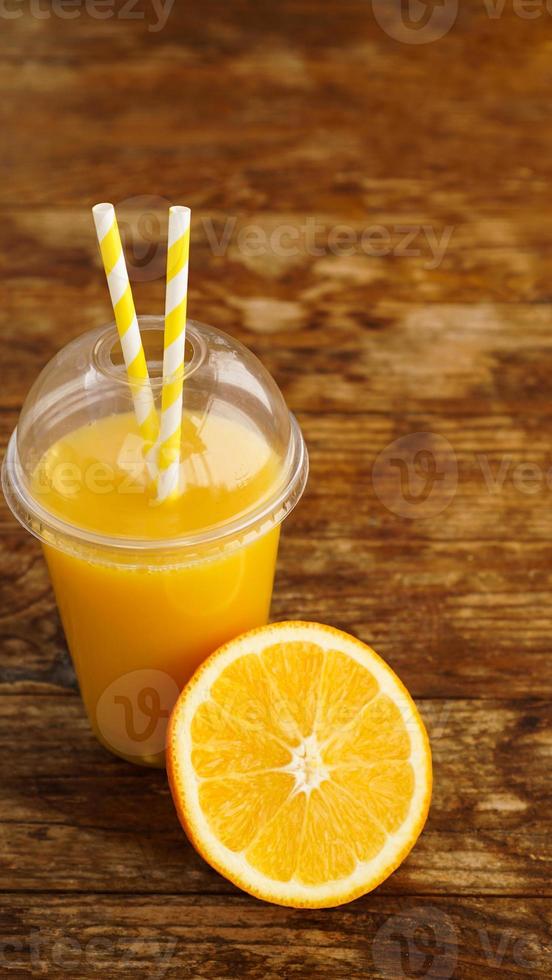 Jugo de naranja en comida rápida taza cerrada con tubos sobre mesa de madera foto